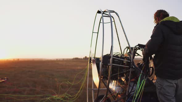 Man Pilot Motor Paraglider Fixes the Parachute To the Body of the Paraglider at Sunset in the Field alt
