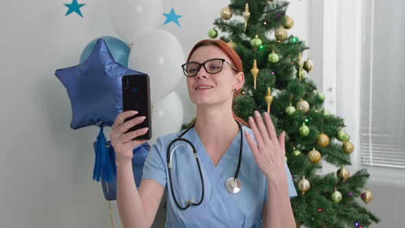 Christmas Online a Charming Doctor Congratulates the Holiday By Video Call Using a Smartphone While alt