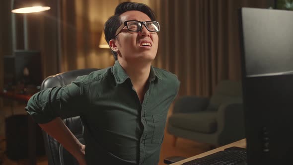 Asian Male Paining His Back While Works On His Personal Computer, He Works Late At Night alt