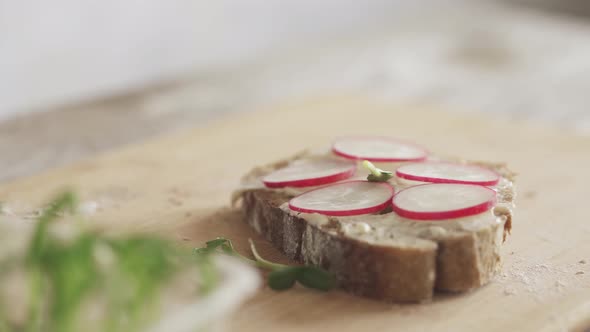 cooking sandwich on board. Slice of bread with bran, soft cheese cheese, fresh radish, microgreens alt
