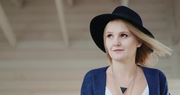 Portrait of a Stylish Middleaged Woman in a Hat on the Terrace of Her House alt
