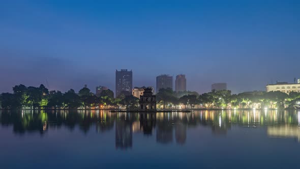 Time lapse of Turtle Tower Temple with skyscraper buildings and reflection in Vietnam. alt