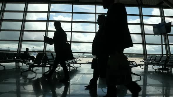 Travelers Walking Along Window in Airport Terminal, People Silhouettes Walking. alt