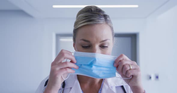 Portrait of caucasian female doctor putting face mask on alt