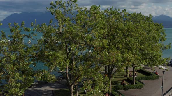 Jib up over green trees revealing a ferry moving over beautiful lake Geneva alt