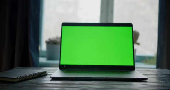 Dolly Push in To Laptop Computer with Green Screen on a Table in Front of Windows with Curtains