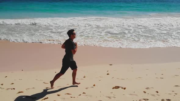 Athletic Man Run Along Ocean Surf By Sandy Beach