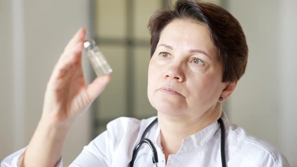 Closeup Portrait of Serious Female Doctor Holding Vaccine Jar and Looking at Camera alt