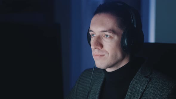 Smiling Businessman Man in Headphones Listening Music and Working at Computer Late at Night