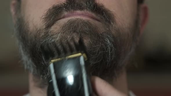 A woman cuts her husband's beard with an electric clipper in the kitchen during quarantine.