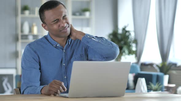 Tired Young African Man with Neck Pain working on Laptop alt