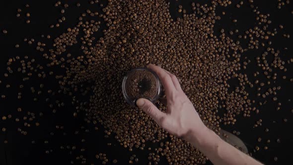 Man Hand Holding Coffee Grinder on Scattered Seeds Background Close Up Top View alt