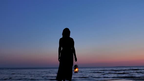 Lonely Female in Dress with Kerosene Lantern Looking at Sunset Sky at Night alt