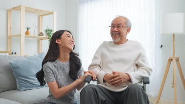 Asian young daughter take care senior male while sitting on wheelchair in living room at home alt