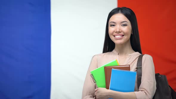 Female Student Holding Copybooks Against French Flag, International Education alt