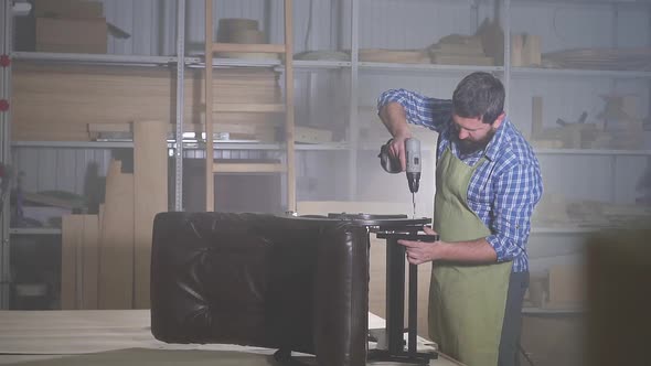 Professional Man with a Beard in a Shirt Is Engaged in Underlaying Assembling a Furniture Chair in a alt