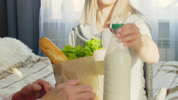 Young Woman Bringing Bag with Groceries to Grandmother