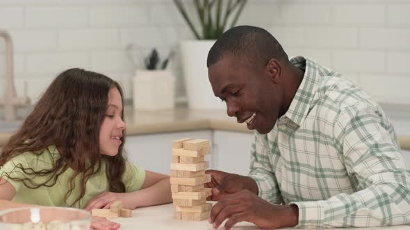 An African American Dad and Daughter are Playing a Board Game at Home Removing Wooden Blocks From a alt
