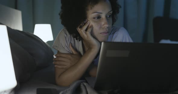 African american woman lying in bed and connecting with her smartphone