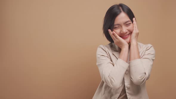 Happy asian business woman feel shy standing with copy space isolated over beige background