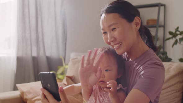 Asian Mom and Baby Daughter Video Calling on Smartphone at Home alt