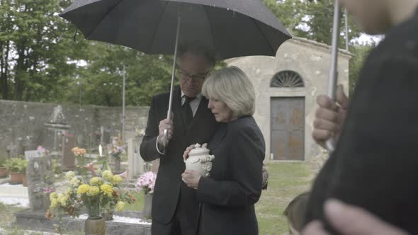 Mourners standing at funeral with cremation urn