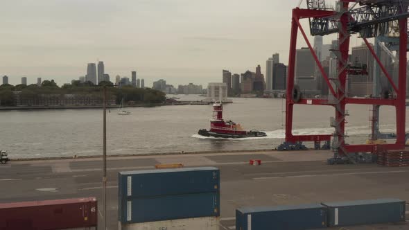 Static Shot of Red Tugboat Driving Past Cranes at the Logistics Container Terminal Pier in New York alt