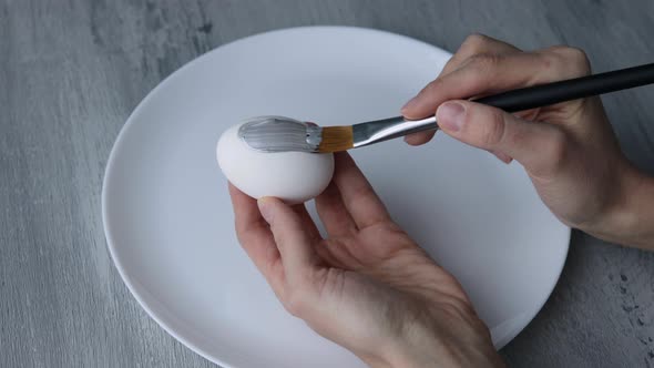 Close-up. Female hands paint Easter egg in a modern minimalist style with colorful paint.