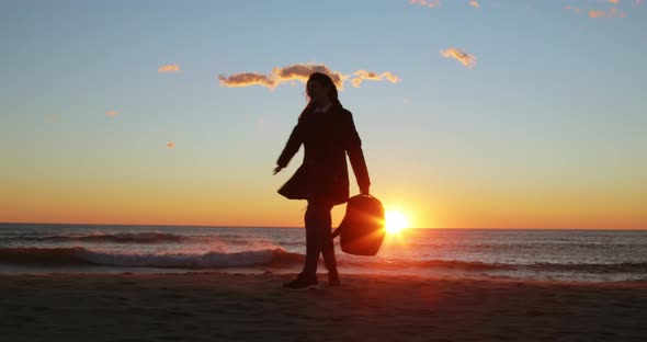 Silhouette of Young Girl with Backpack Cheerfully Dances at Sunrise on the Beach alt