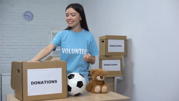 Smiling Volunteer Putting Clothes and Toys in Box, Helping Orphans, Donation alt