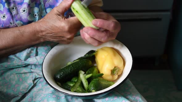 Old Woman Peels Cucumber with Knife in Her Wrinkled Hands