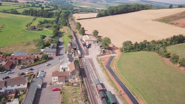 Drone shot tracking forward over a village and train station, with a Diesel engine at the station. S alt