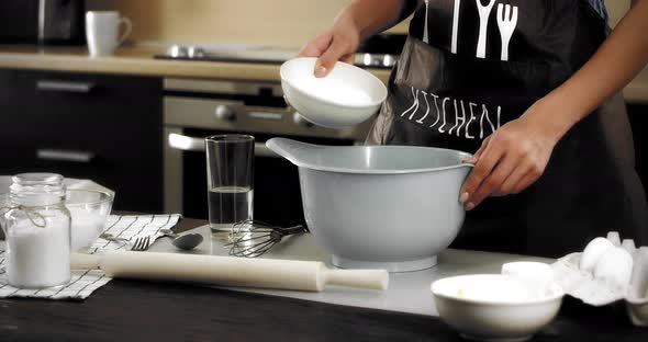 Woman in an Apron Pours Sugar Into a Gray Bowl in a Modern Kitchen