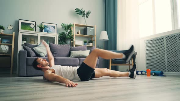 Active Guy Exercising at Home Doing Sports Lying on Floor Raising Legs and Arms alt
