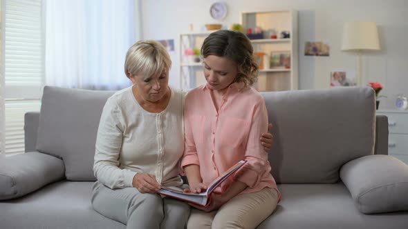 Sad Adult Female Looking Through Family Photobook Together With Mother, Memories alt