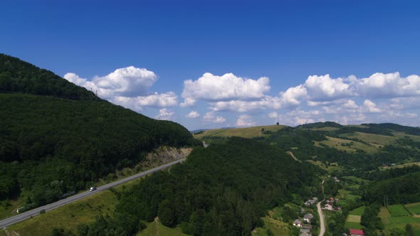 Truck Driving on the Asphalt Road in a Rural Landscape With Forested Mountains Aerial View