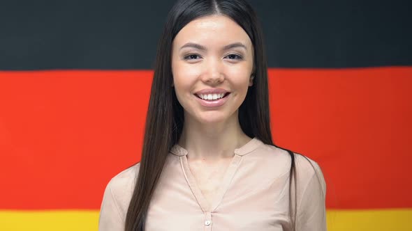 Smiling Asian Woman Showing Passport, Standing Against German Flag, Citizenship alt