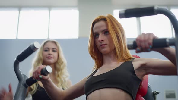 Concentrated Redhead Sportswoman Training Hand Muscles on Equipment with Cheerful Blurred Personal alt