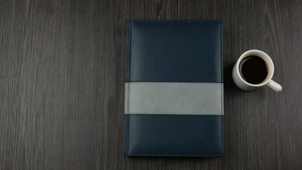 Grey Covered Notepad and Cup of Cofee on Dark Wooden Background. Opening a Notepad for Writing alt