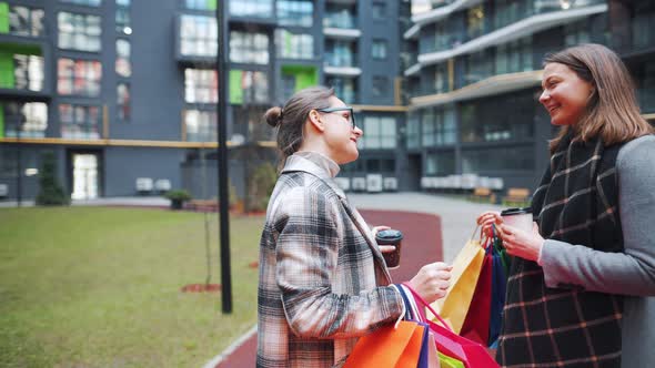 Two Happy Women Stand with Shopping Bags and Takeaway Coffee After a Successful Shopping and Talk alt