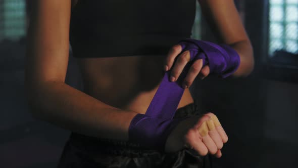 Closeup View of Muay Thai Female Boxer Wrapping Bandages on Her Hands Before Fight in Dark Room with alt