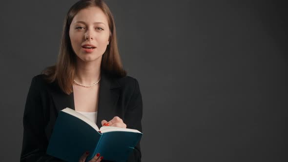 Young Woman in Black Suit Listens to the Collocutor with Smile and Makes Notes to the Paper Notepad alt
