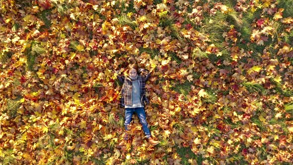 Aerial view A Cute Little Girl Lies in the Park on Yellow Fallen Leaves. alt