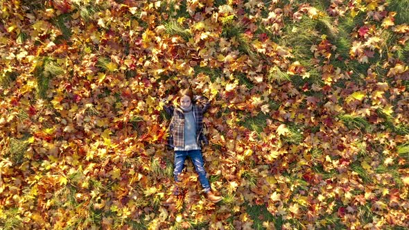 Aerial view A Cute Little Girl Lies in the Park on Yellow Fallen Leaves.