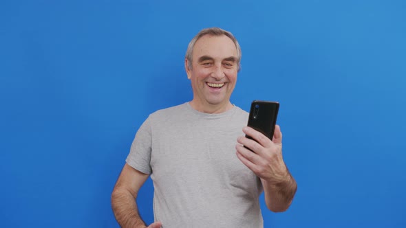 Happy Senior Elderly Man Holding Smart Phone Watching Mobile Video Calling Online Looking Screen alt