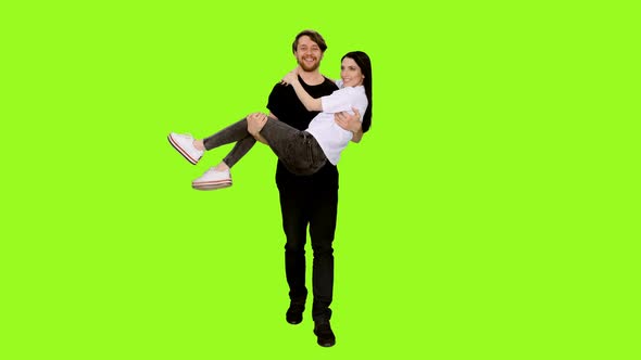 Happy Young Man Carrying Girlfriend in His Arms Against Green Background