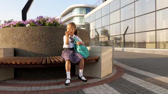 Little Pupil in School Uniform is Eating Apple on Bench alt
