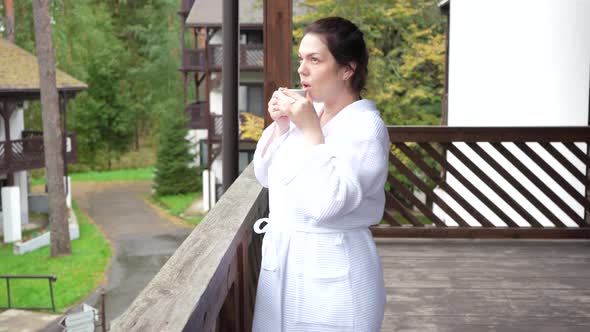 A Girl in a White Coat Goes Out on Balcony in Morning to Drink Coffee in Fresh Air