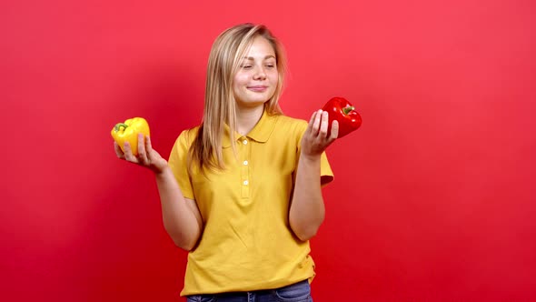 Cute and Slightly Fat Girl in a Yellow T-shirt Holding a Yellow and Red Pepper in Her Hand. alt