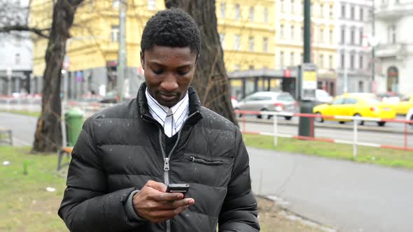 Young Handsome Black Man Works on Smartphone - Urban Street with Cars - City alt